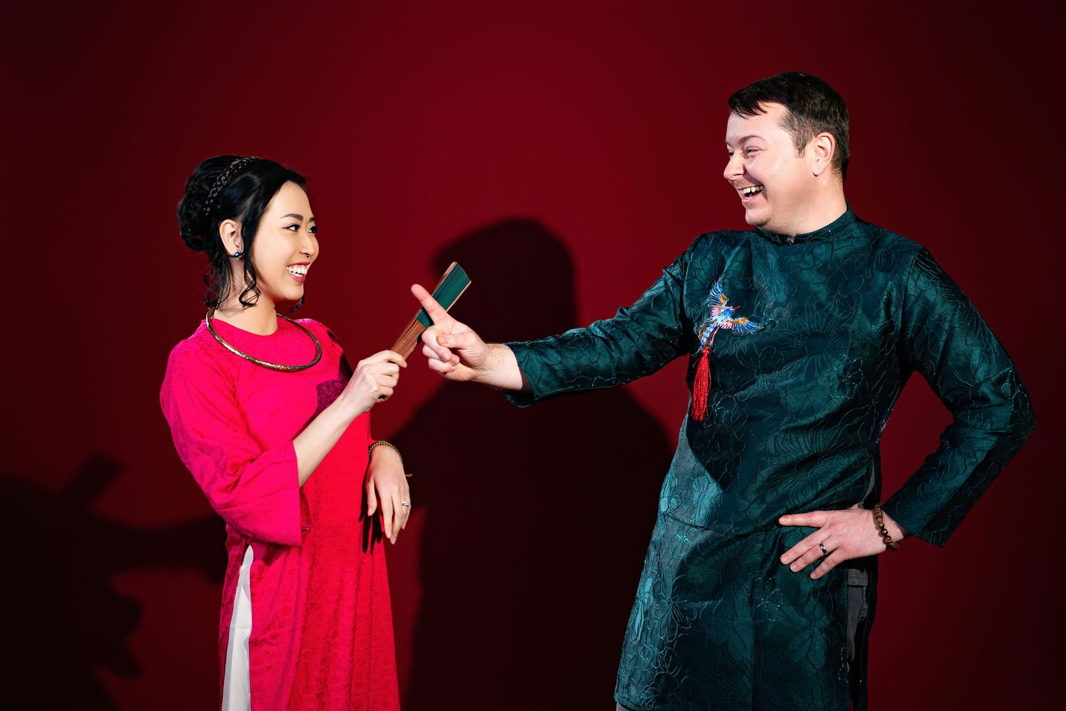 Couple in traditional Asian and western attire performing dramatic poses against red backdrop.