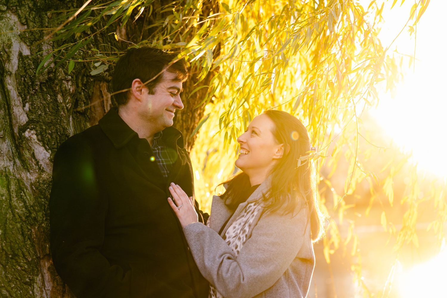 Romantic couple embraces in golden sunlight during sunset photoshoot in outdoor setting.