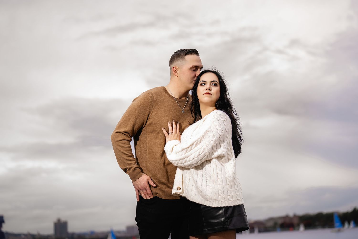 A couple embraces while standing together outdoors on an overcast day.