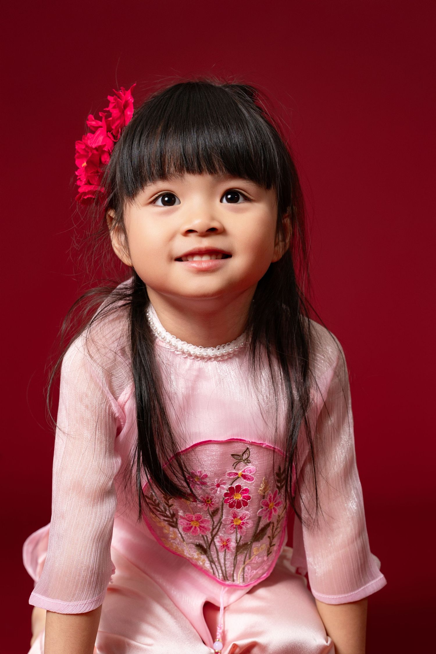 A series of photos showing a child in a pink traditional Chinese dress with floral embroidery against a red backdrop.