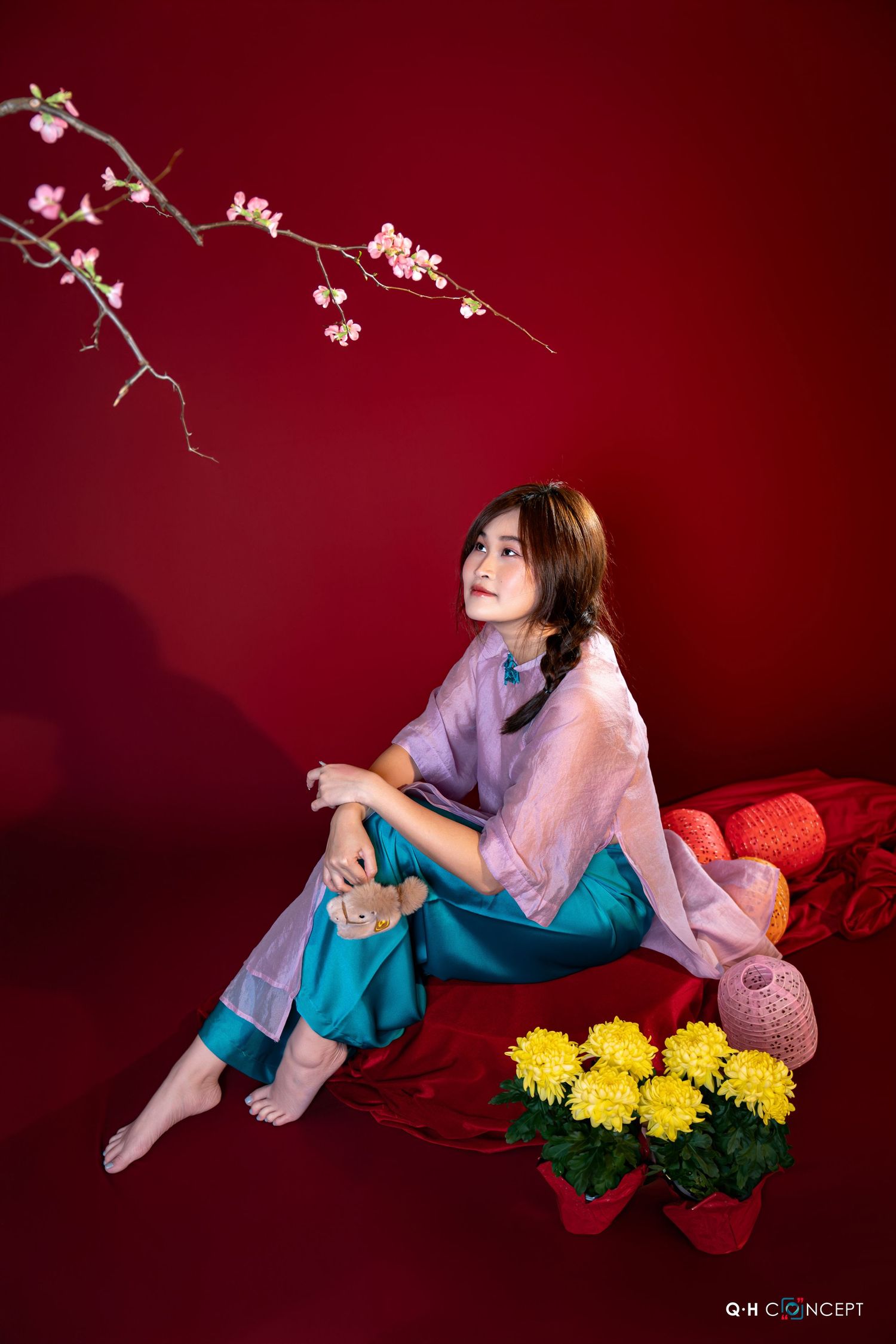 Fashion portrait against red backdrop with yellow chrysanthemum flowers and flowing pink and teal garments.