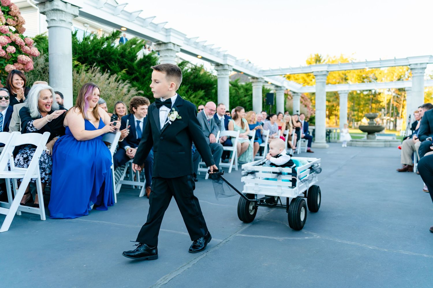 Outdoor wedding venue with white columns and guests gathering on a patio at sunset.