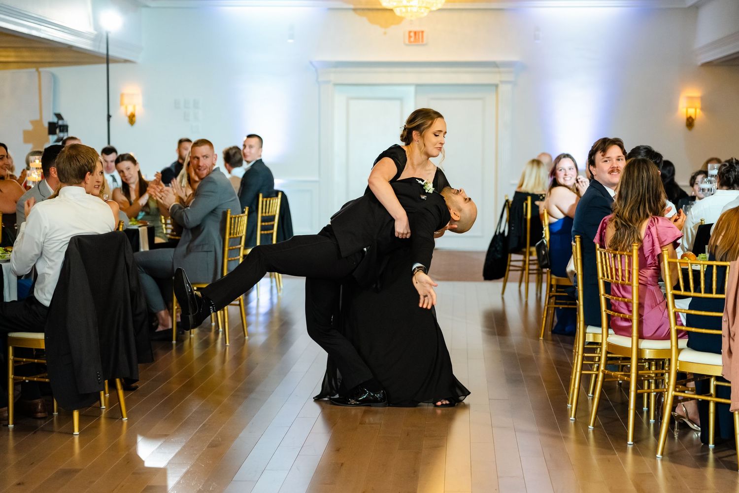 Panoramic view of a wedding reception venue with guests dancing and mingling in a bright white ballroom.