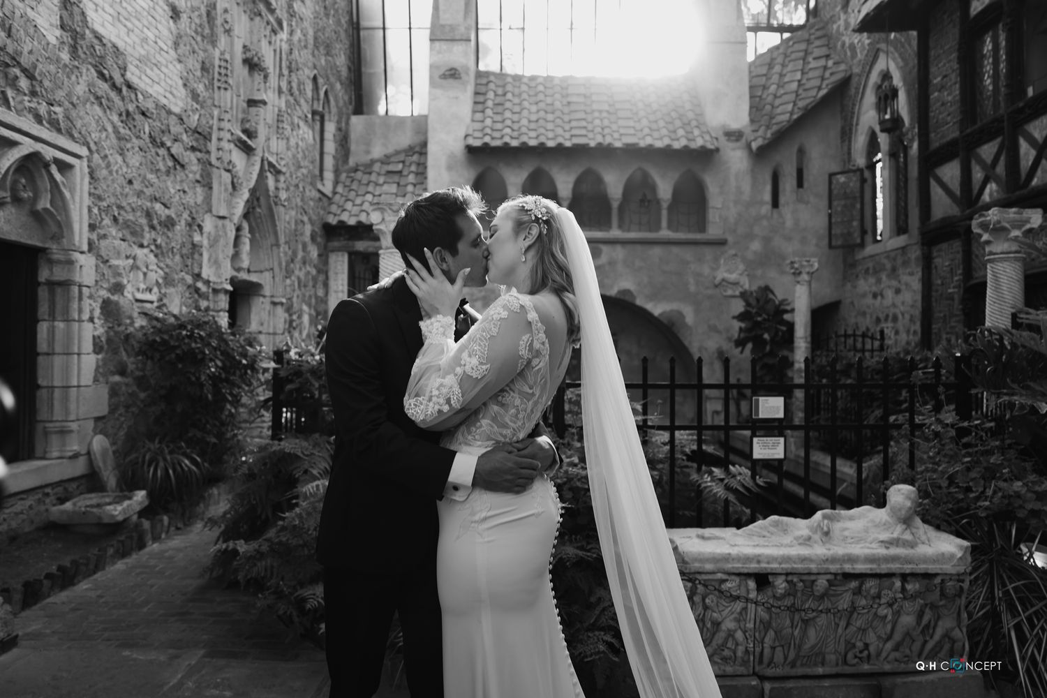 A wedding couple poses in a stone archway with dramatic natural lighting.