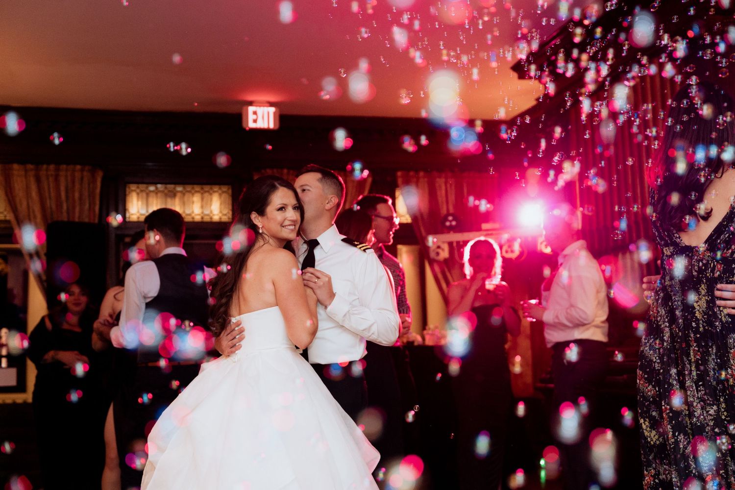 Wedding reception dance floor filled with guests under pink lighting and falling confetti creating a festive atmosphere.