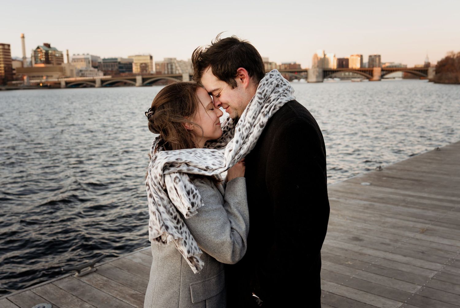 A couple shares an intimate moment on a dock by the water at sunset, creating a romantic silhouette against the sky.