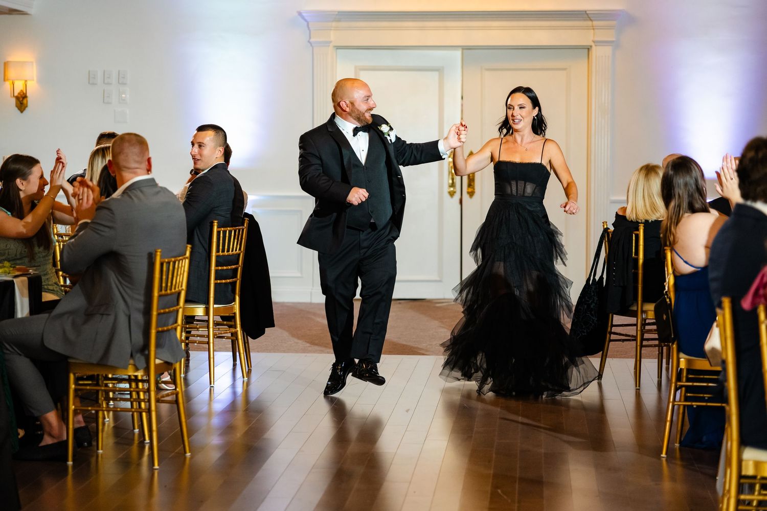 Wedding couple makes energetic entrance into reception hall with guests seated along the aisle.