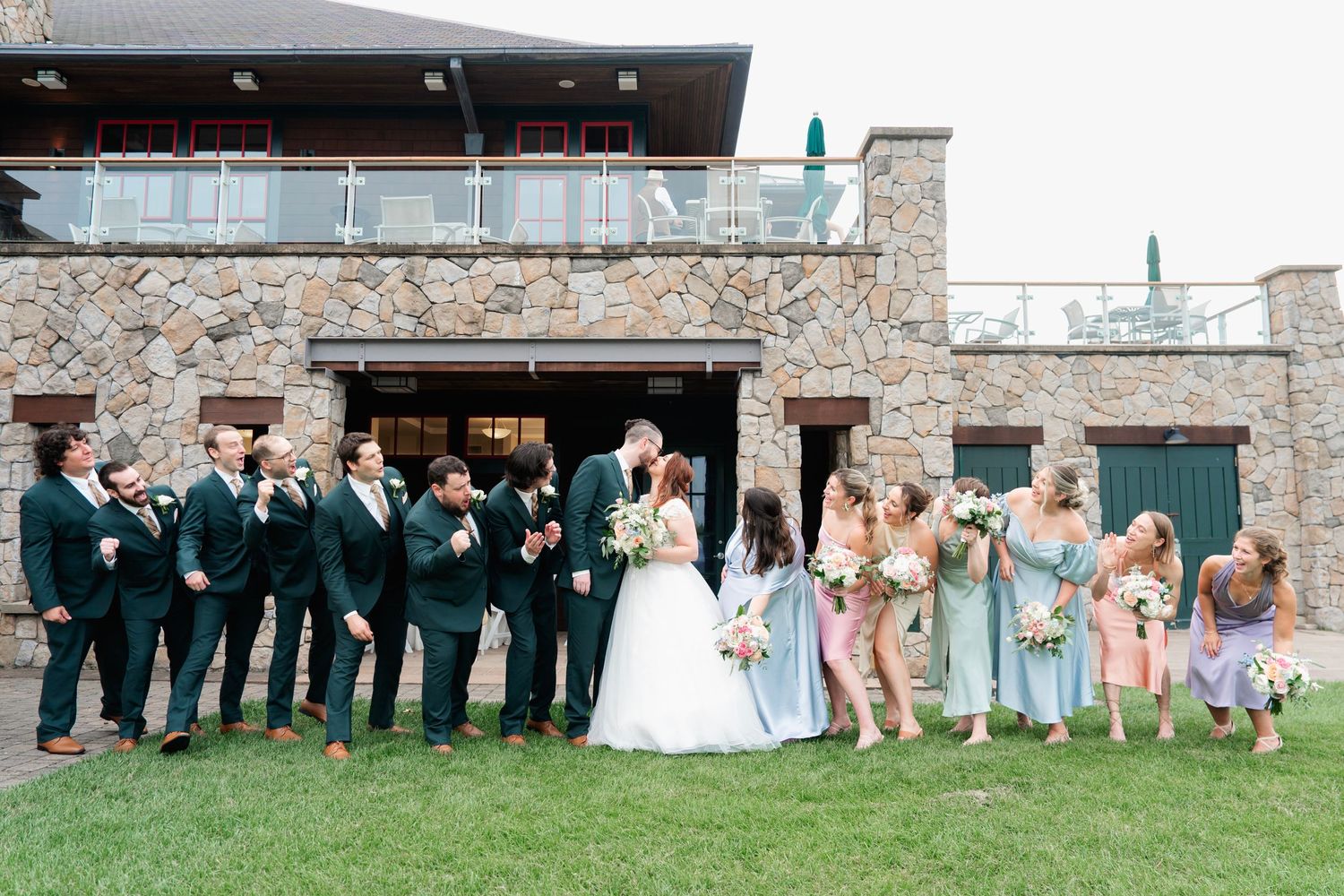 Wedding party poses against rustic stone wall exterior for formal group photos.
