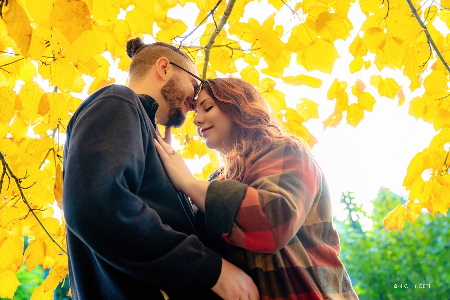 Intimate moment captured under bright yellow autumn leaves during outdoor photoshoot.