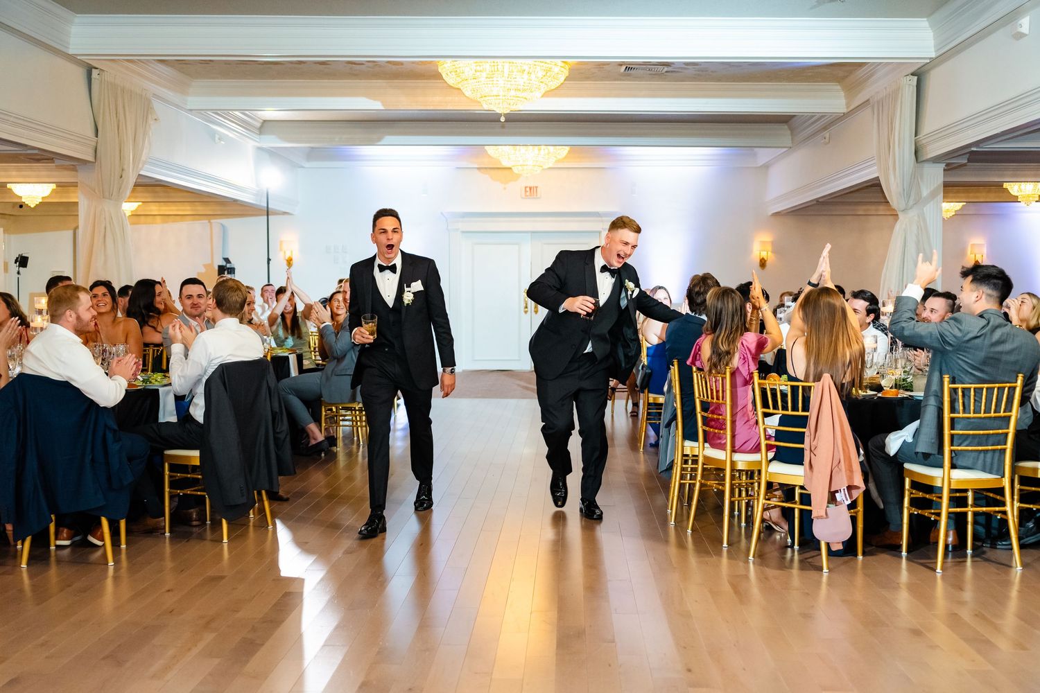 Wedding party members make dramatic entrance into reception hall with guests seated at tables.
