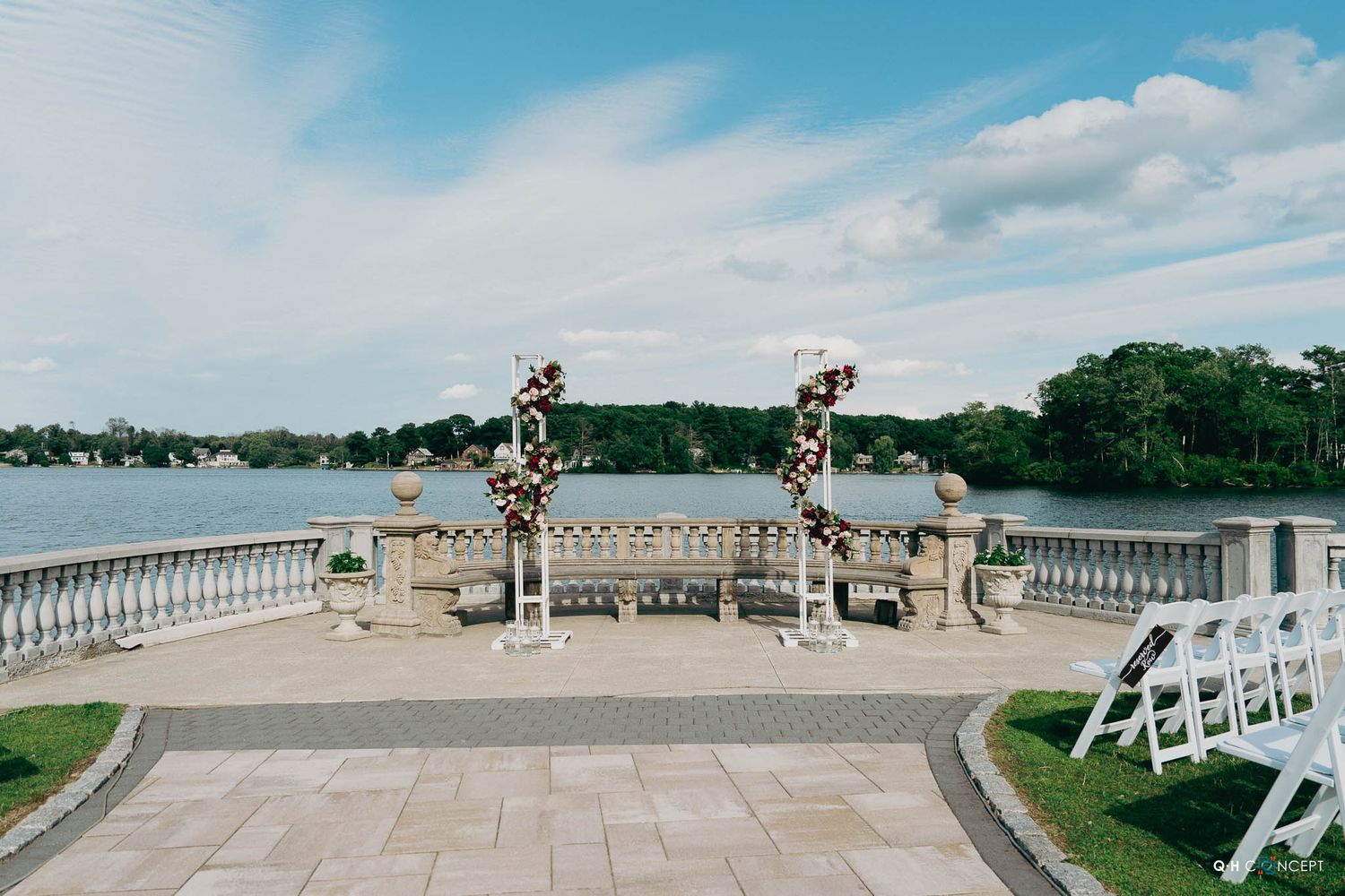 Ornate stone balcony with decorative pillars and floral arrangements overlooking a waterfront landscape.