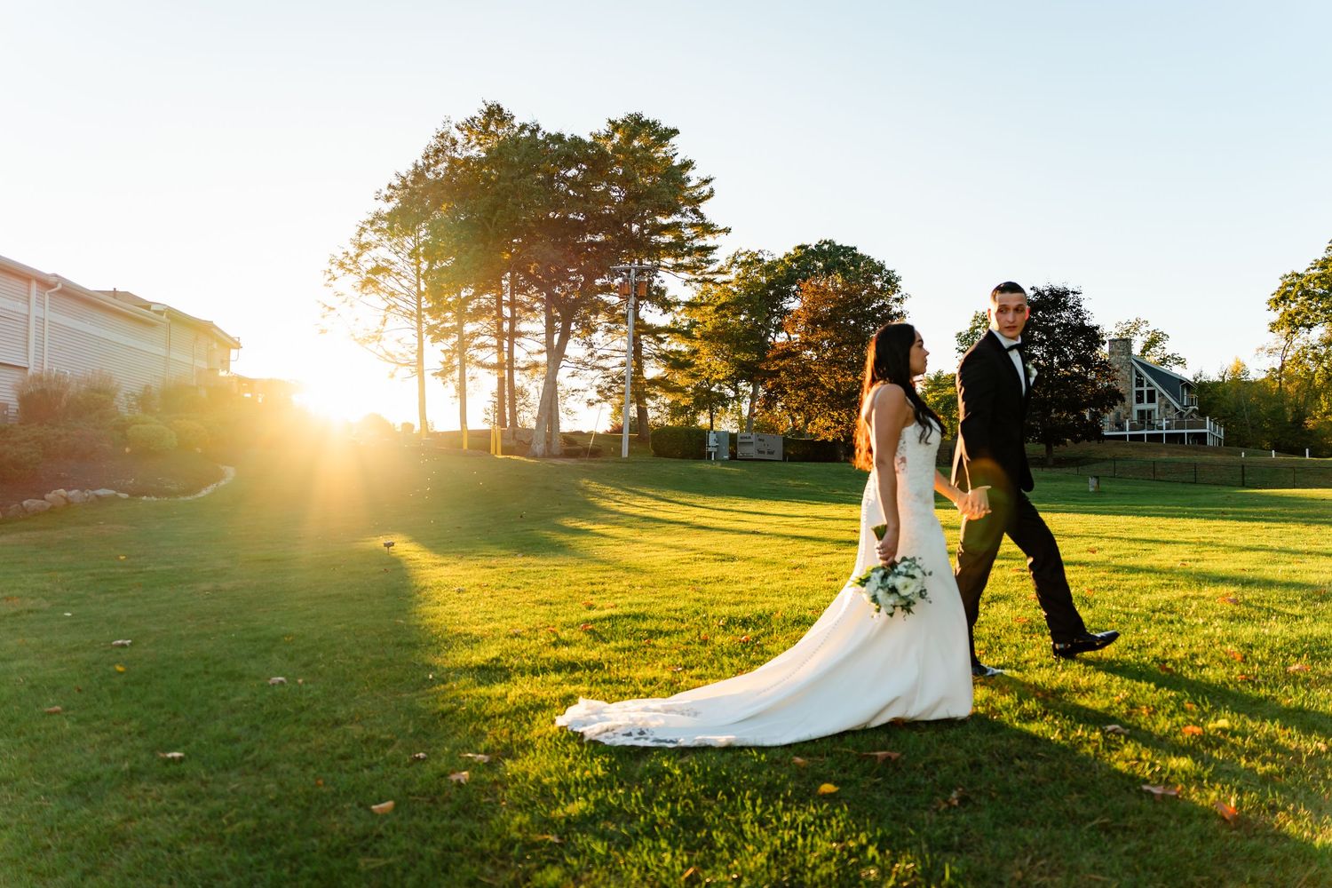 Wedding couple poses in golden sunlight on a grassy hill during sunset.