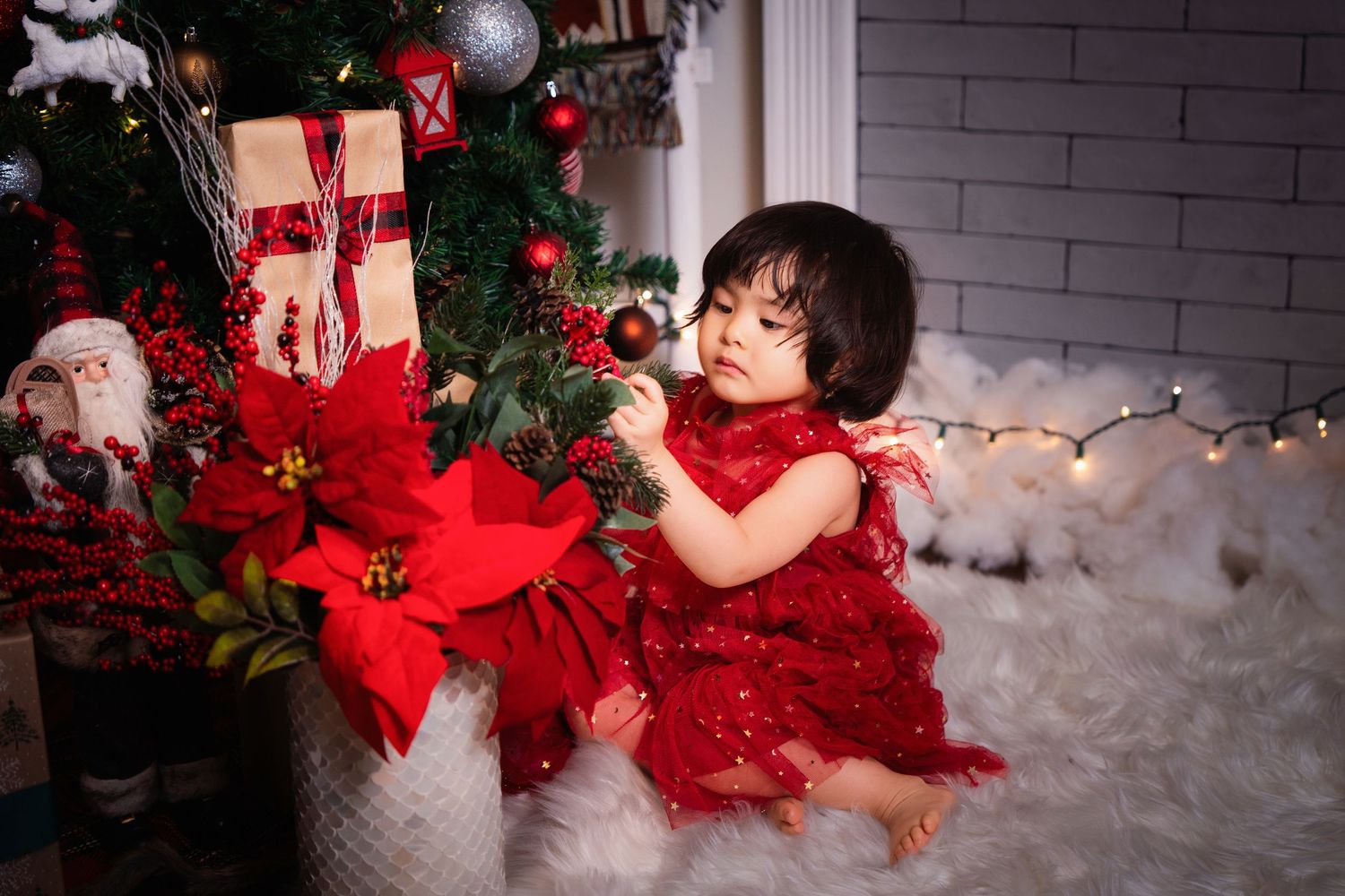 A festive holiday photo session featuring red dresses and Christmas decorations against a white brick wall backdrop.