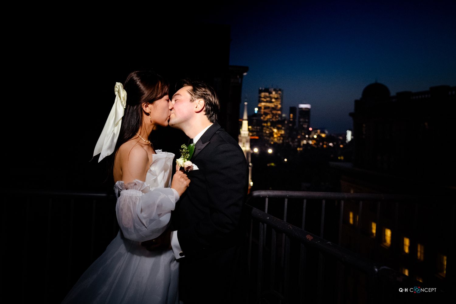 A silhouetted couple embraces on a beach during sunset with city lights in the background.