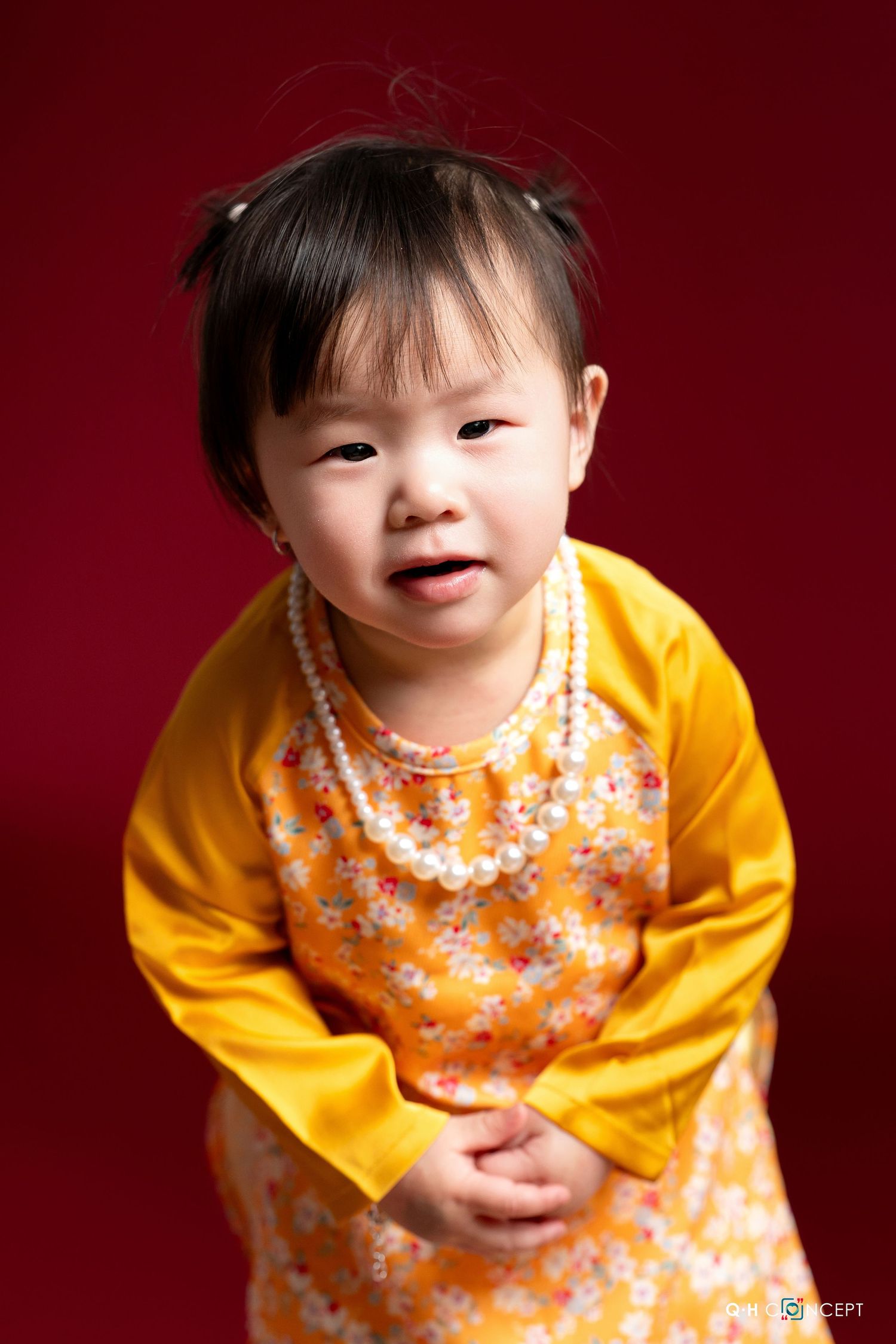 A series of photos showing a child in a yellow cardigan and floral dress against a deep red background.