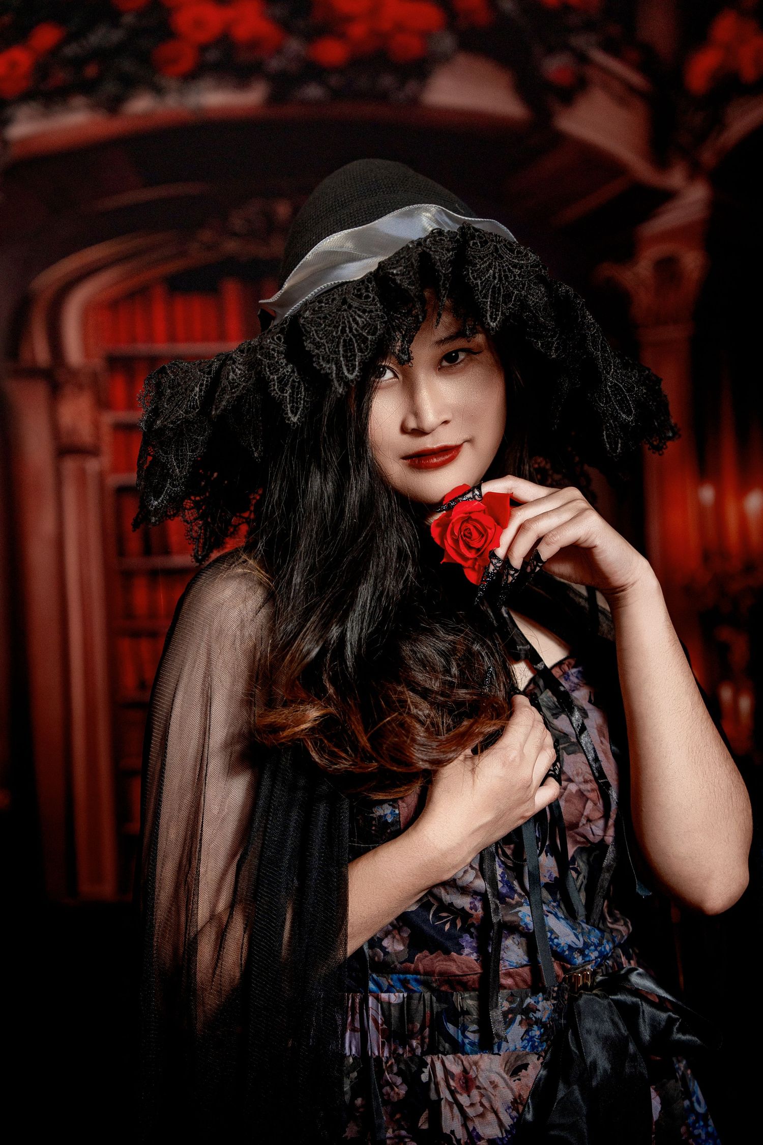 Gothic glamour shot with red rose and black lace against dark library setting.