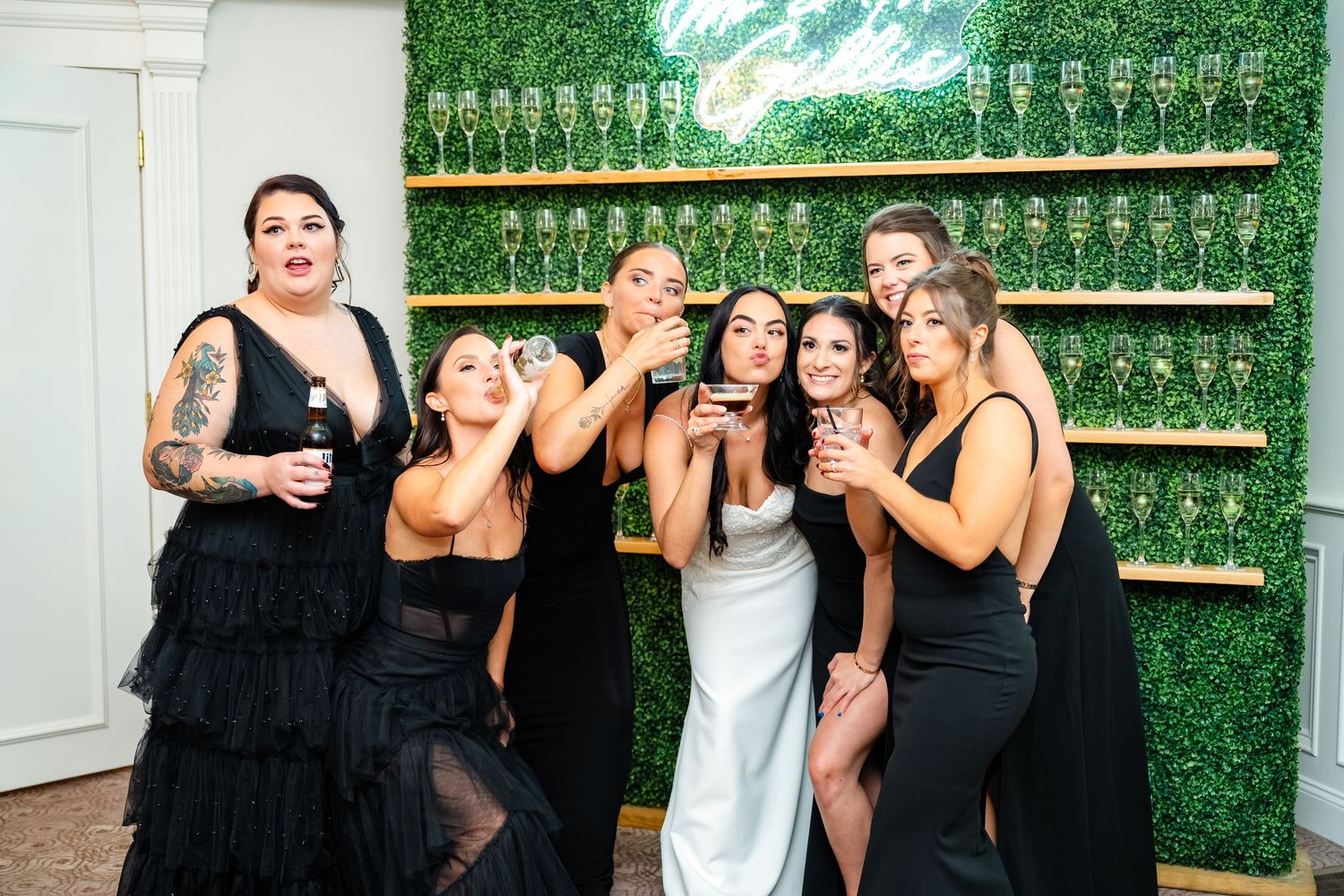 Group poses together against green bottle wall backdrop at wedding celebration.