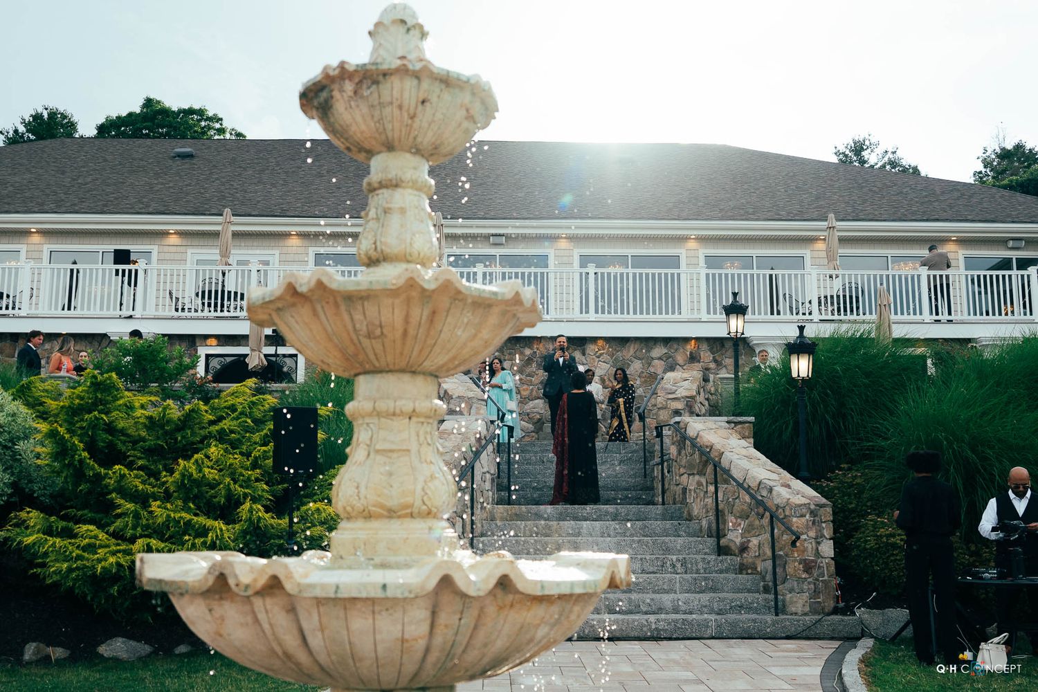 Elegant tiered fountain stands before stone steps leading to a white colonial-style building with balcony.