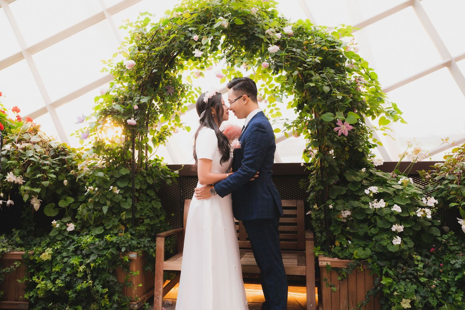 Wedding ceremony setup under an elegant vine-covered pergola with white decor.