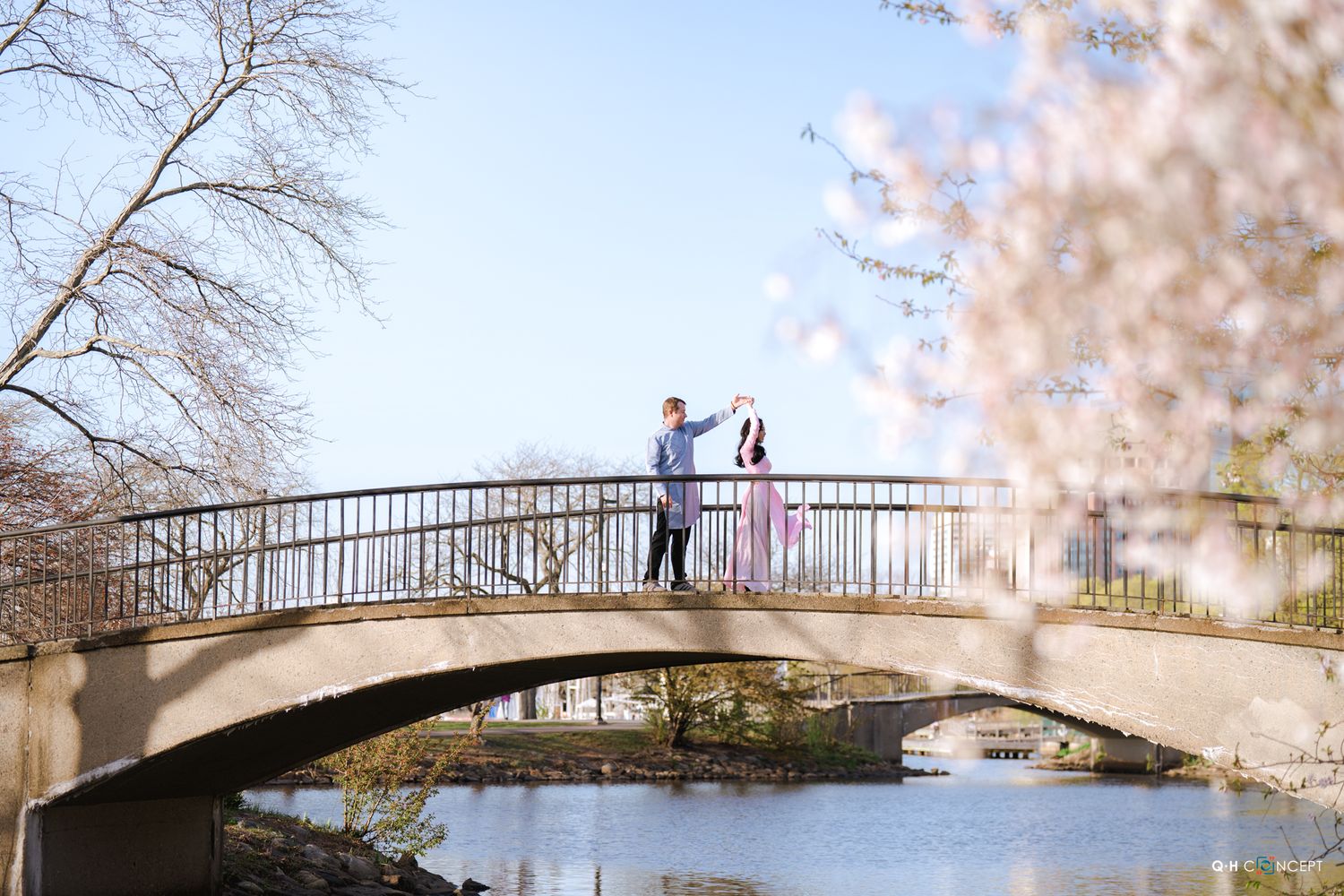 Couple standing on a stone bridge surrounded by cherry blossoms in bloom on a sunny spring day.