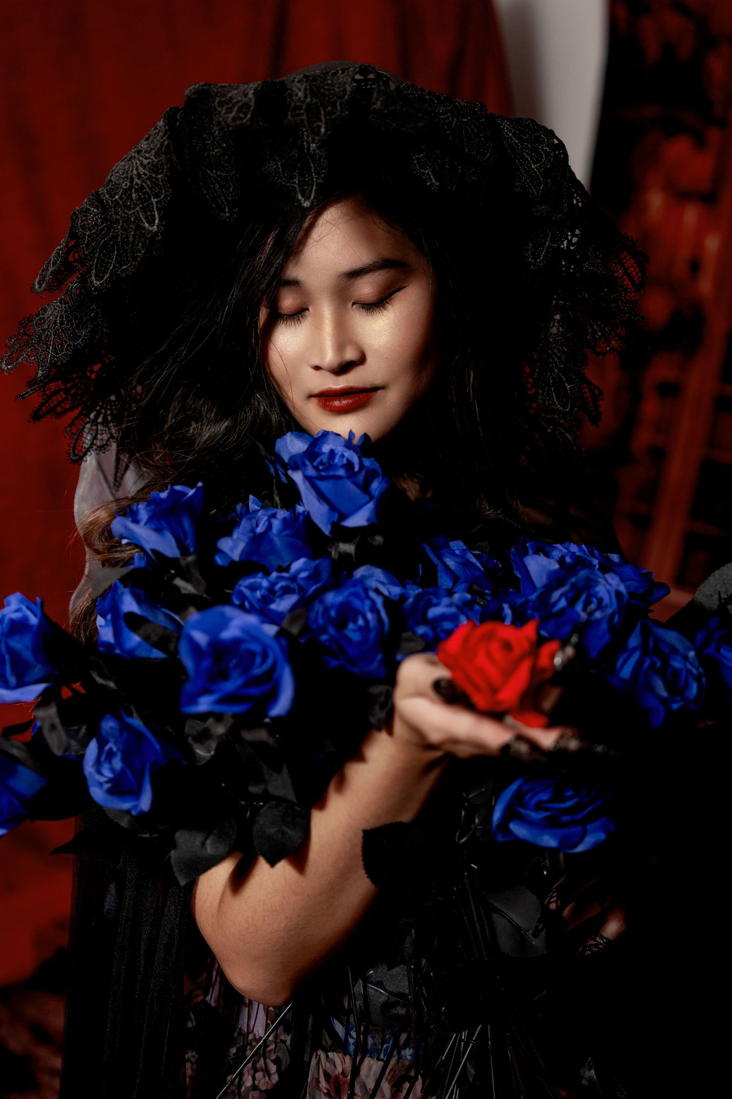 Dramatic portrait with blue roses against red backdrop and black lace.