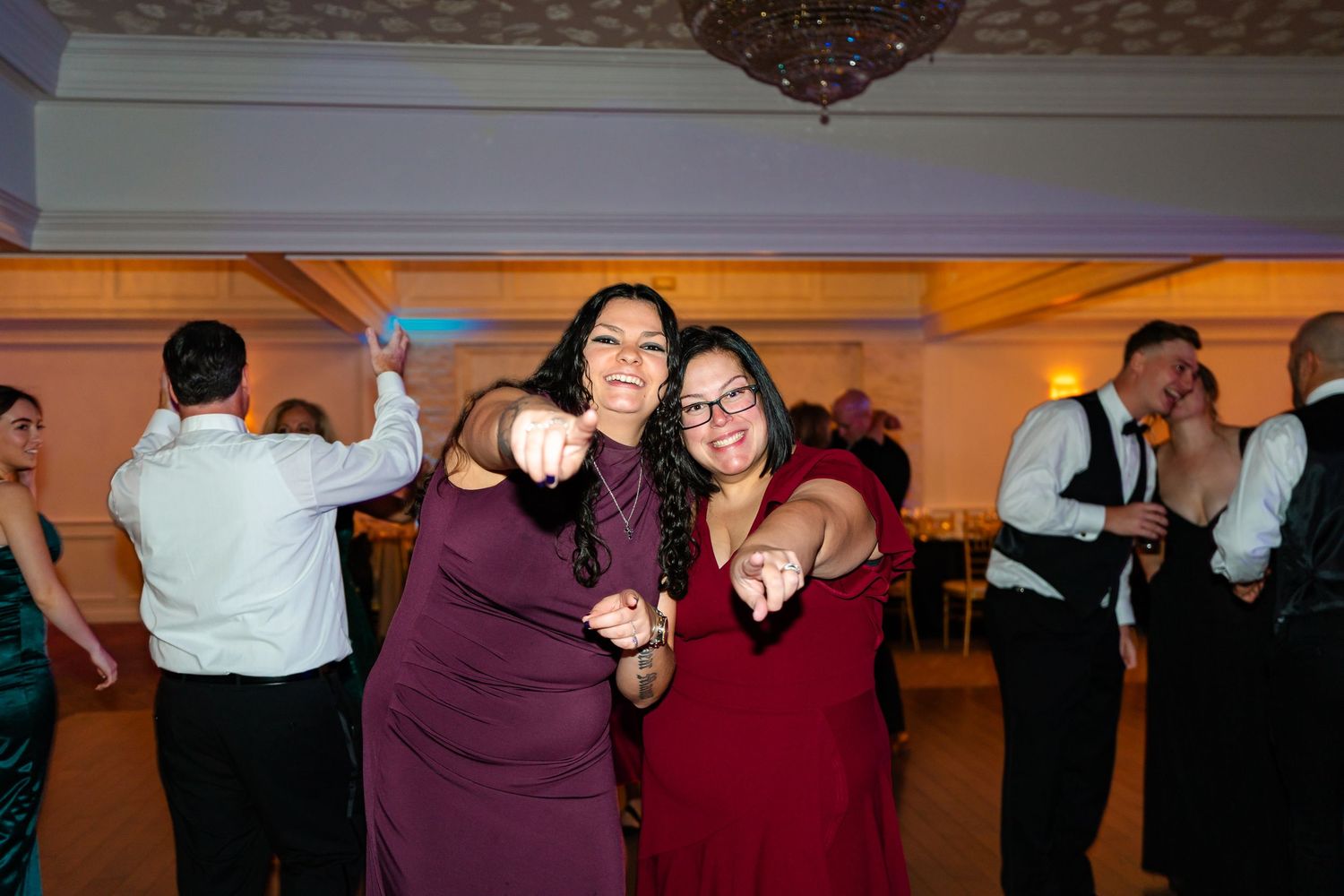 Wedding reception guests dancing and celebrating in a dimly lit ballroom.