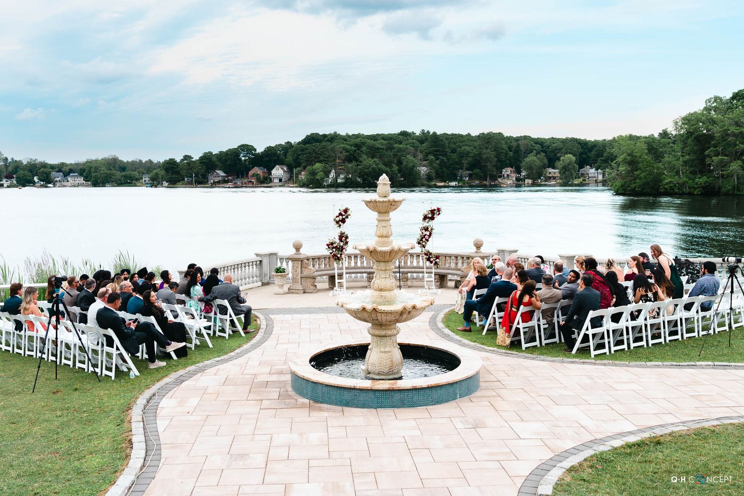 Outdoor wedding ceremony setup with white chairs arranged around an elegant fountain overlooking a serene lake.