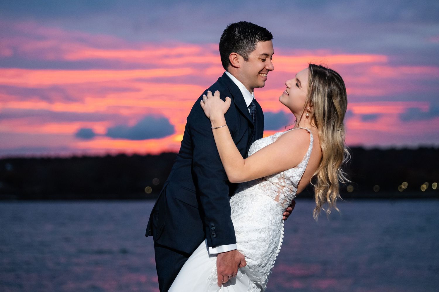 Romantic sunset photoshoot by the water with vibrant pink sky.
