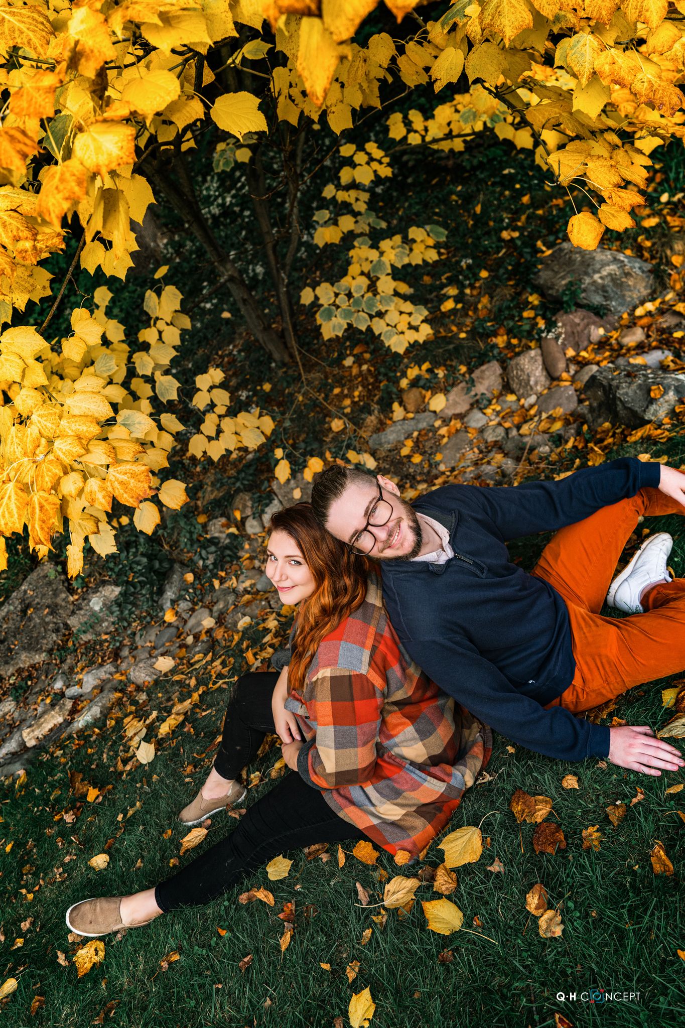 Couple lying on grass beneath golden yellow fall foliage during autumn photoshoot.