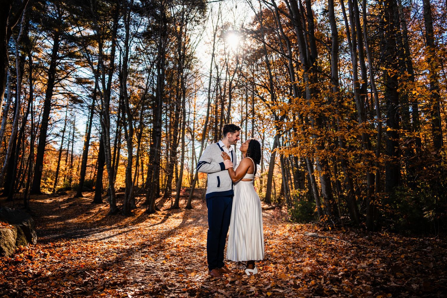 Couple standing together on an autumn forest path surrounded by golden trees and sunlight.