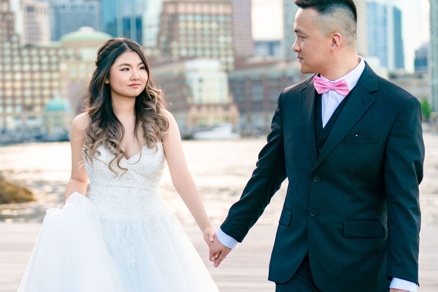 A couple poses against an urban cityscape backdrop in formal attire.