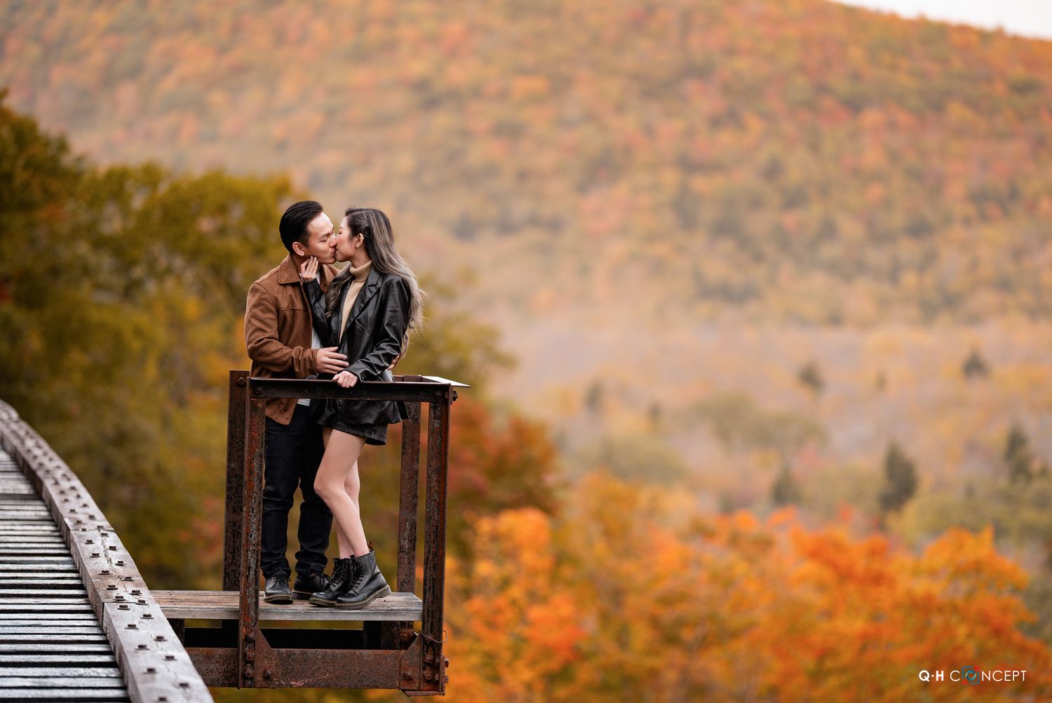 A couple shares an intimate moment on wooden planks with autumn mountains in the background.