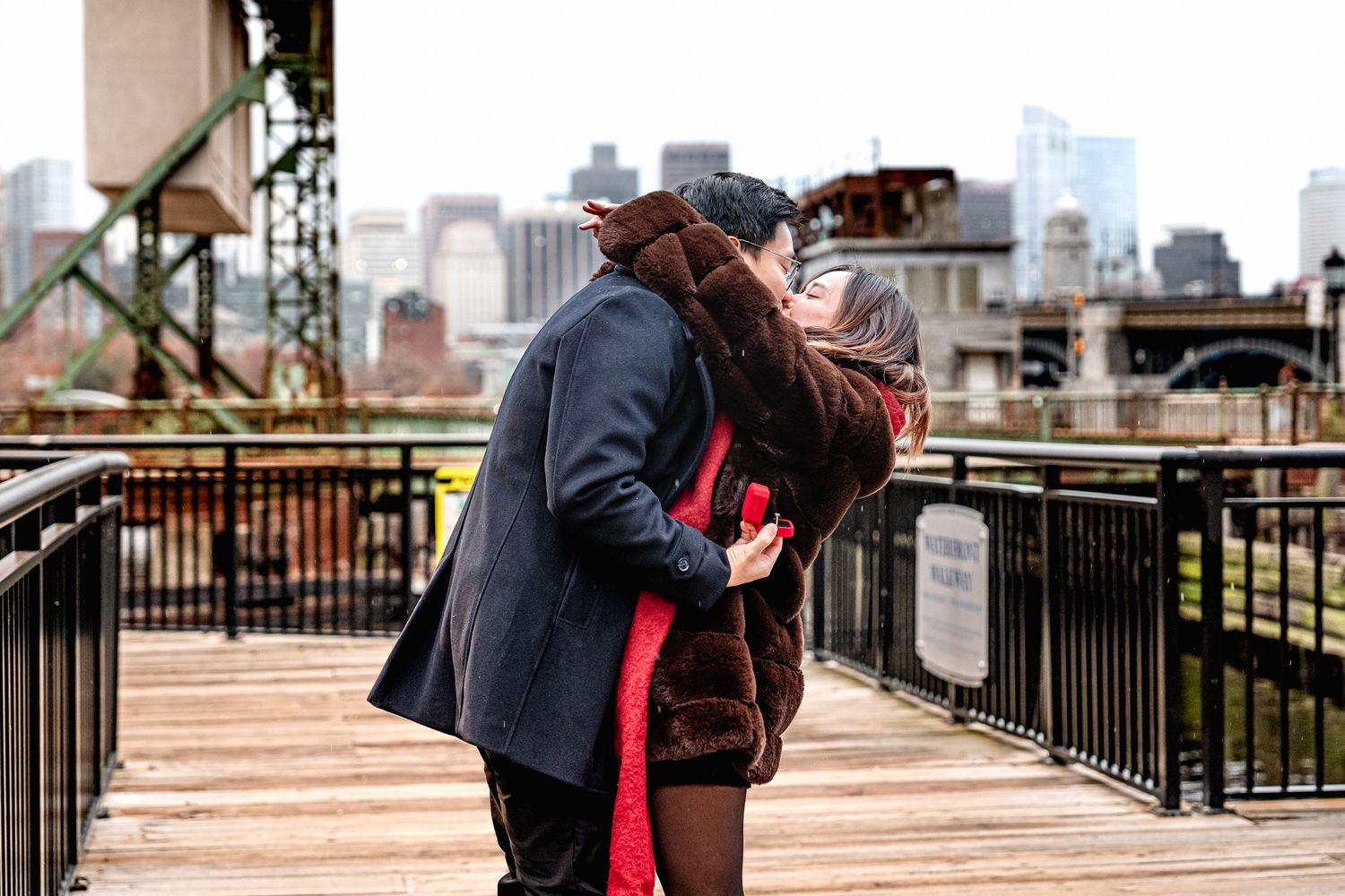 Couple embraces on a city rooftop terrace with urban skyline and buildings in the background.