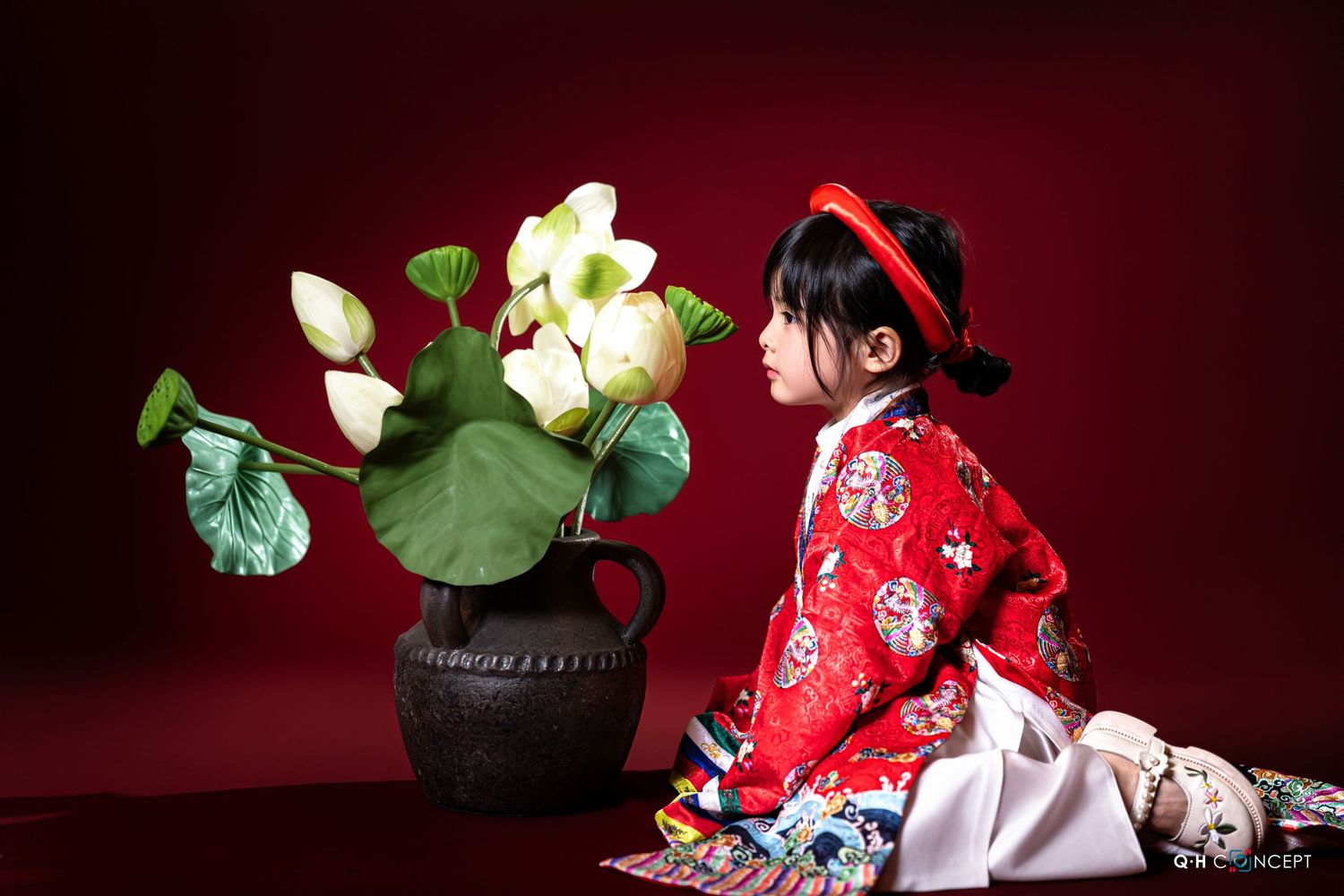 A red kimono-clad figure poses with white lotus flowers against a deep burgundy background.