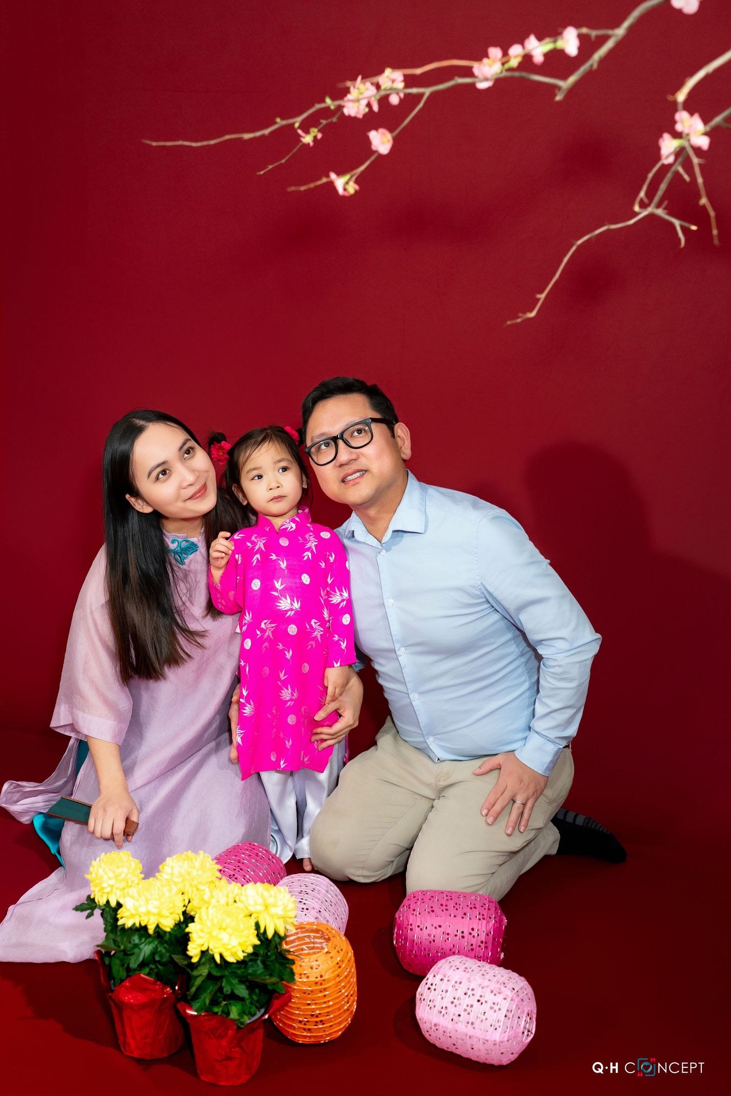 Family poses with colorful lantern decorations against festive red backdrop for Lunar New Year celebration.