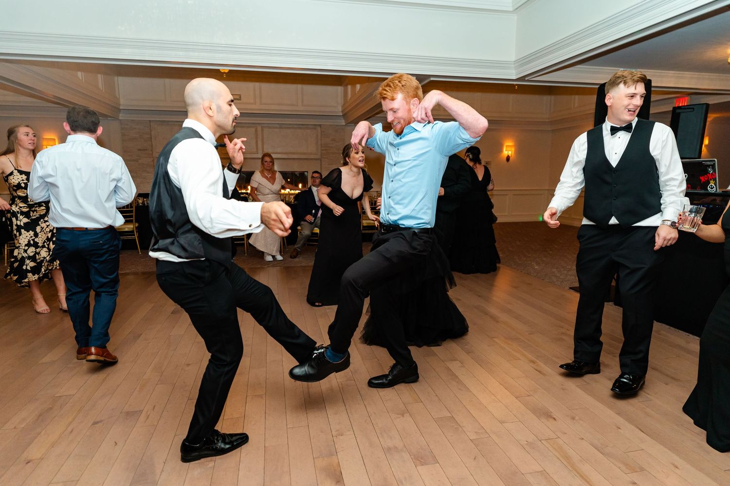 Groomsmen performing synchronized dance moves on a wooden dance floor at the reception.