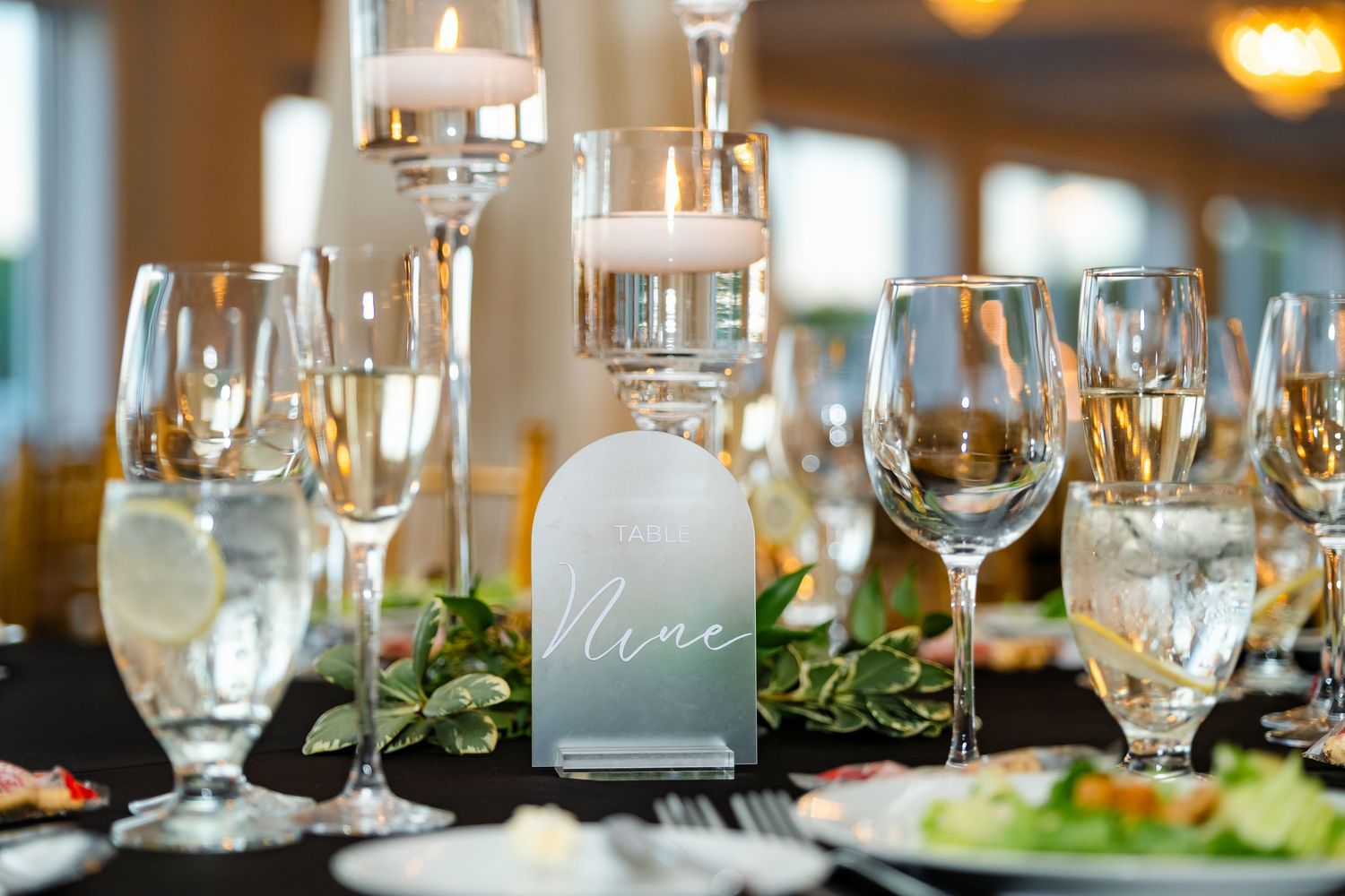 Elegant table settings with wine glasses and greenery at a formal dining event.