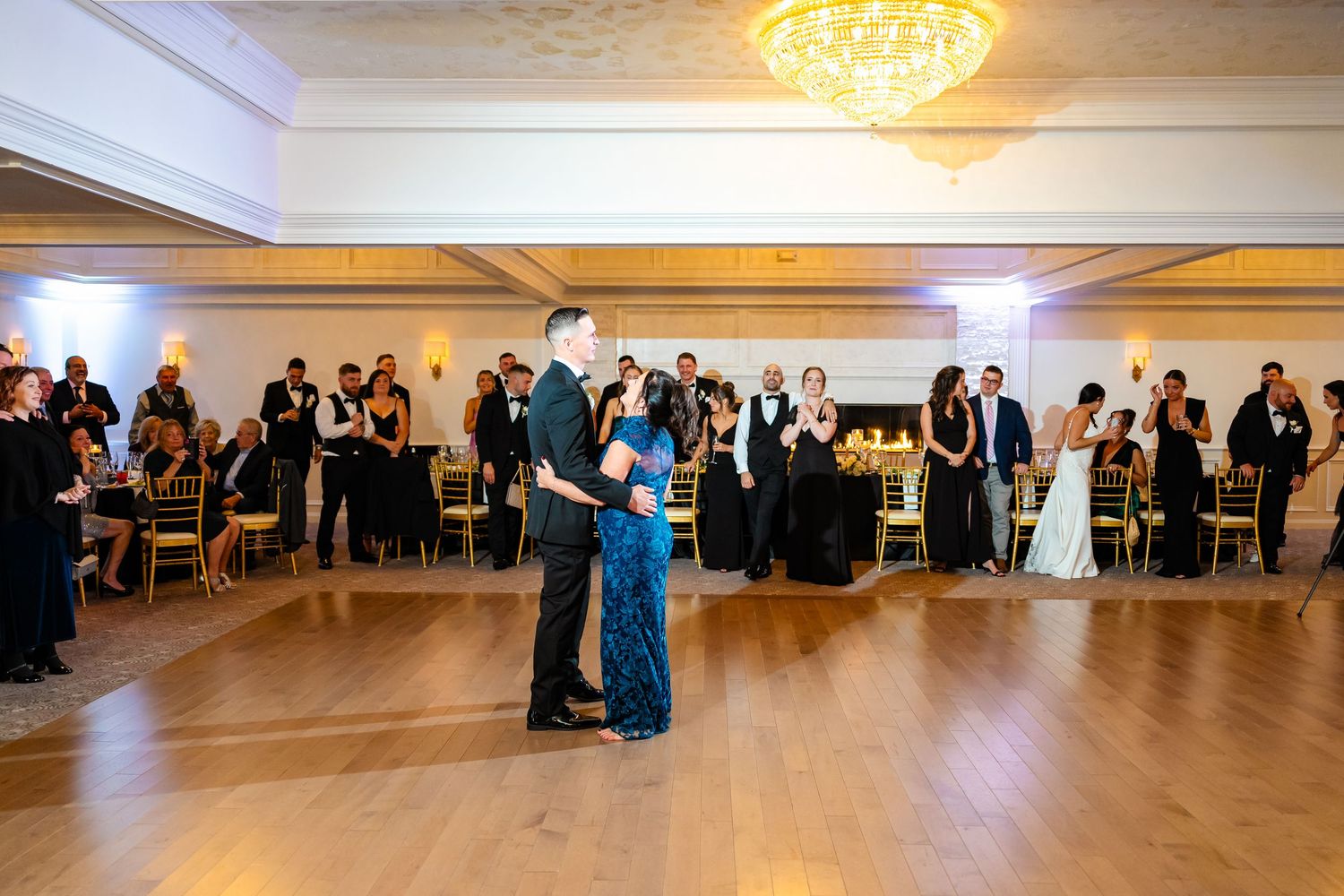 Wedding guests dancing together on a large ballroom dance floor under elegant chandeliers.