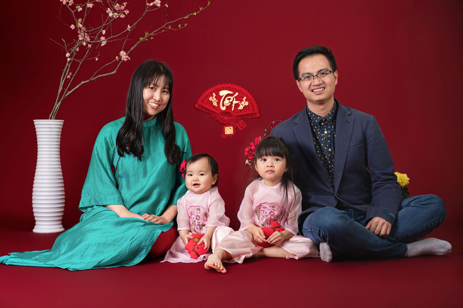A family in traditional Chinese New Year attire sits together on a red backdrop with decorative elements.
