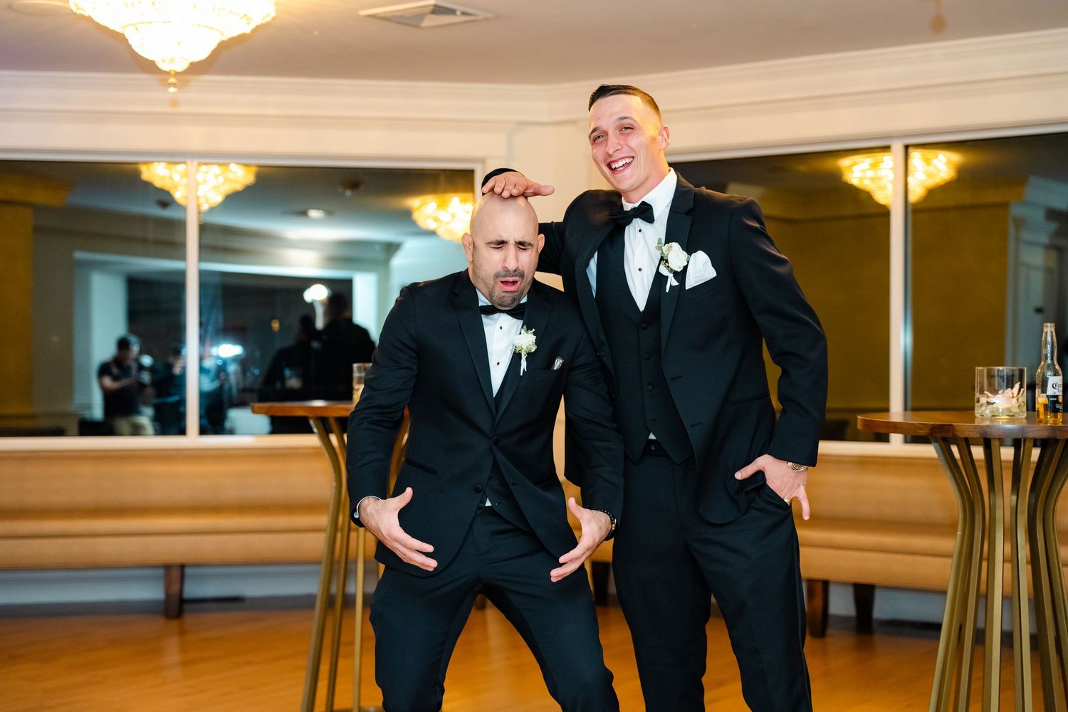 Groomsmen in black tuxedos performing choreographed dance moves at wedding reception.