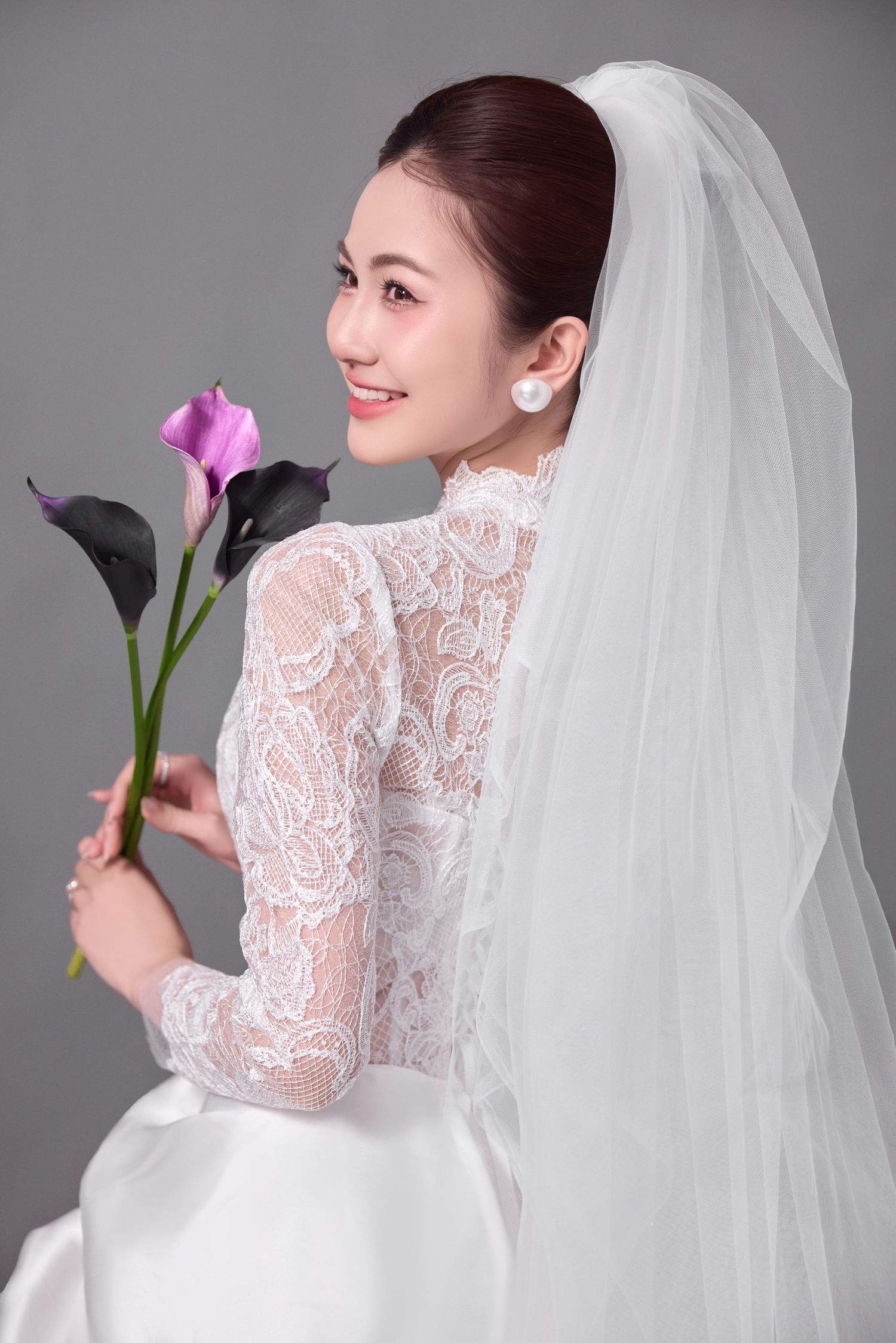 An elegant lace wedding gown with flowing veil photographed against a grey backdrop.