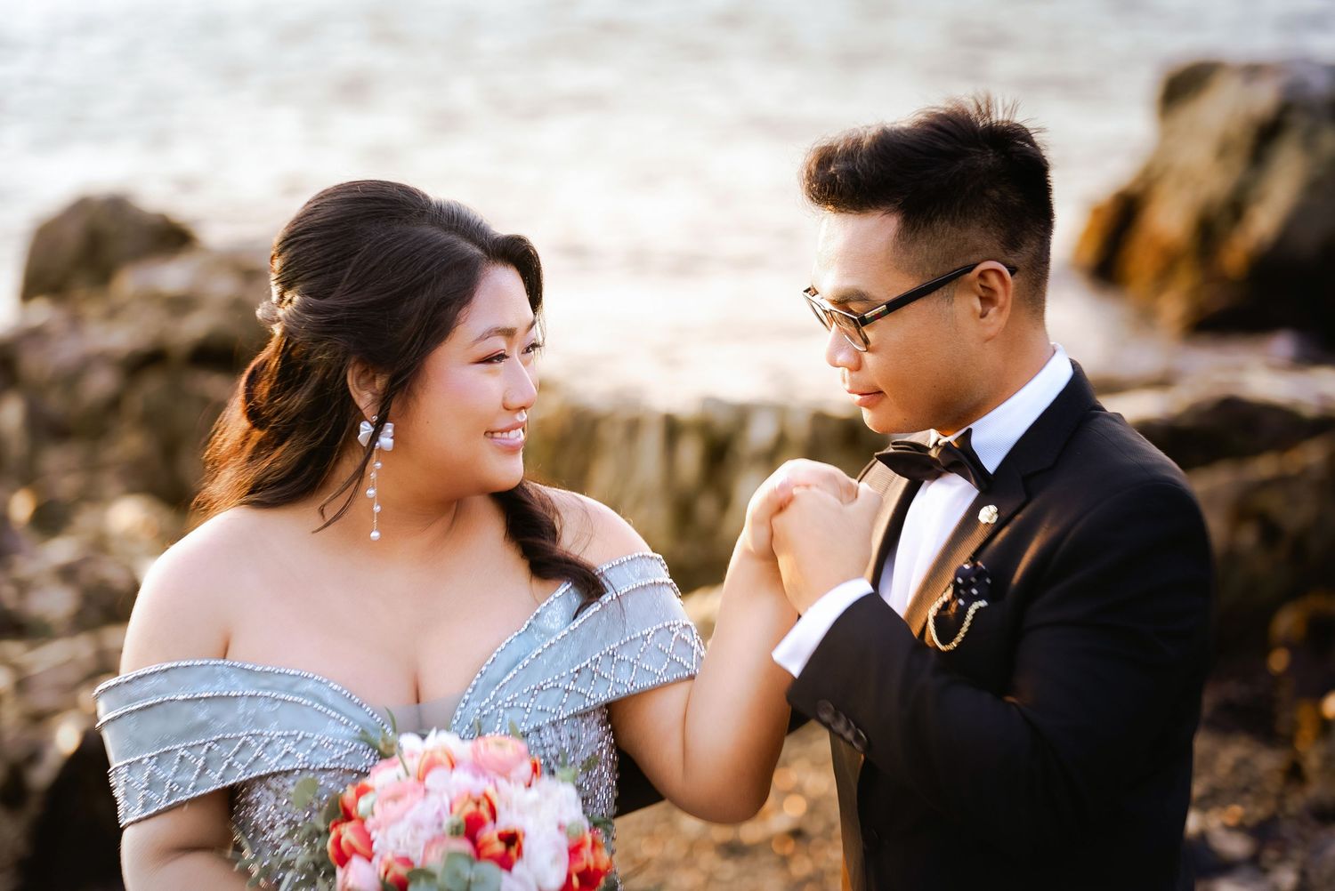 A couple shares tender moments at sunset wearing formal attire on a rocky beach.