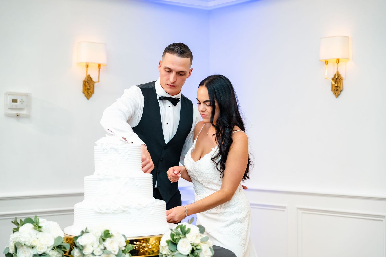 Wedding reception venue decorated in white and blue lighting with elegant wall sconces.