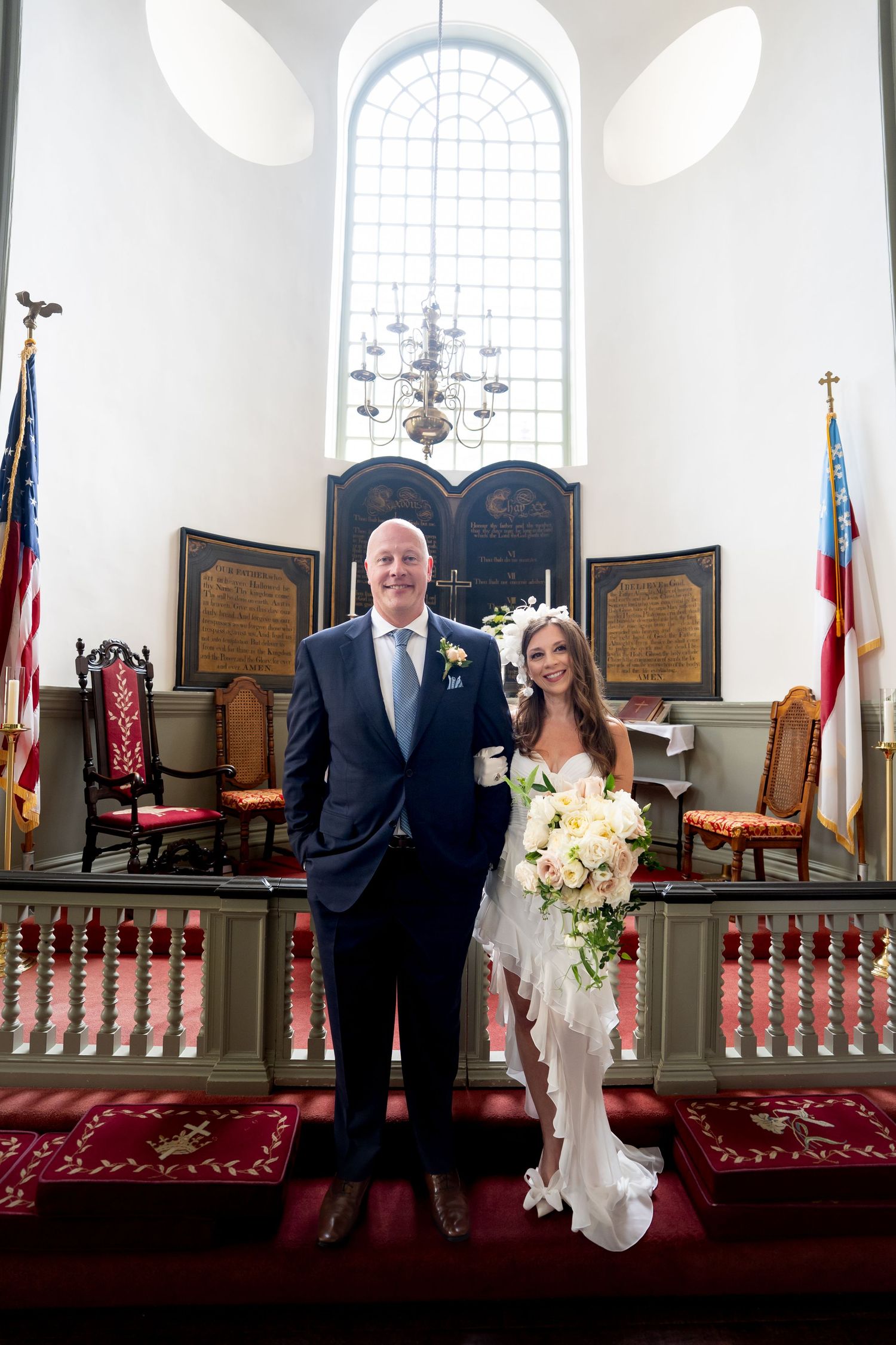 A wedding ceremony takes place in a traditional church sanctuary with arched windows and red carpeting.