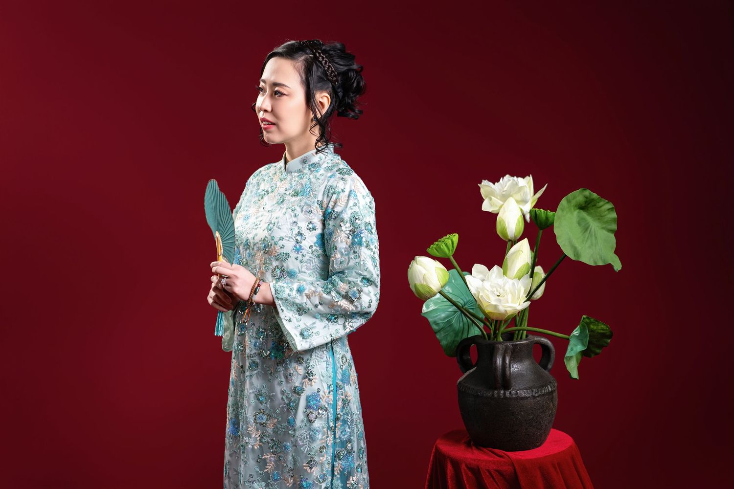 A woman in a traditional blue floral hanbok poses gracefully against a deep red background with white flowers.