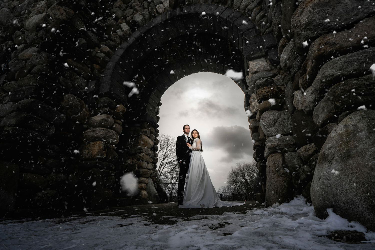 A wedding couple poses against dramatic black rock formations at sunset in an outdoor setting.