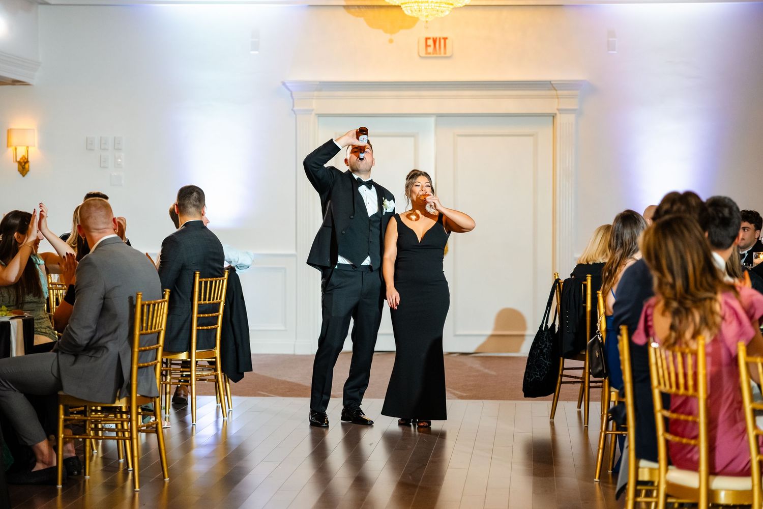 A couple makes their grand entrance at a wedding reception with guests seated in gold chairs.