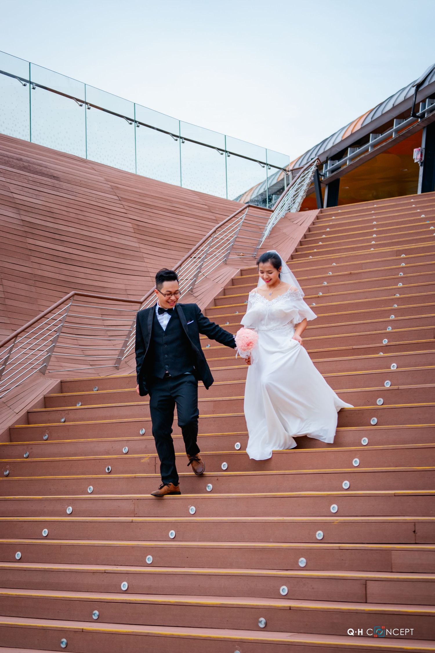 A couple descends modern wooden amphitheater-style steps in formal attire.