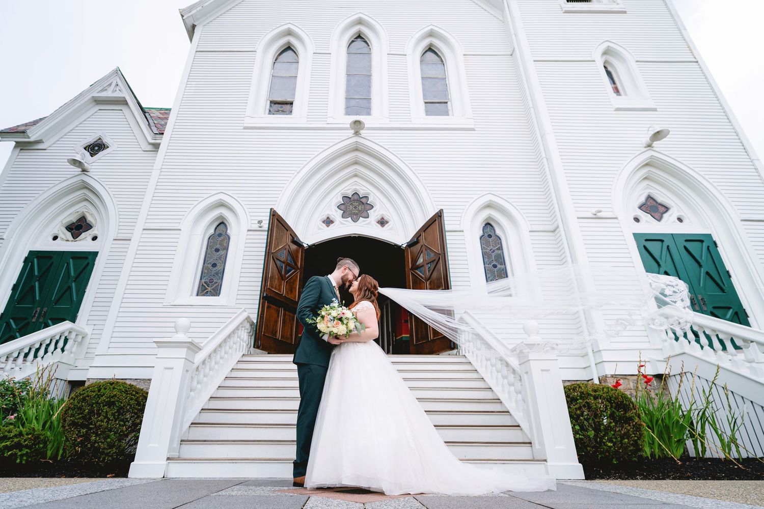 A white church exterior with gothic architecture features and stone steps leading to the entrance.