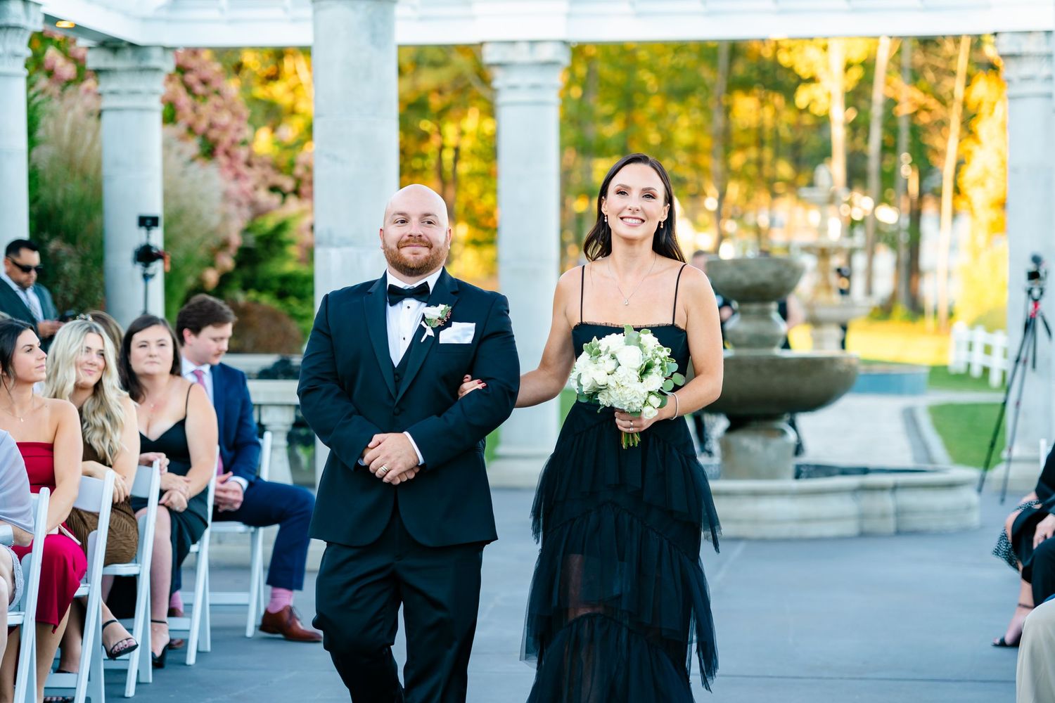 Wedding ceremony setup outdoors with white chairs and columns against autumn foliage.